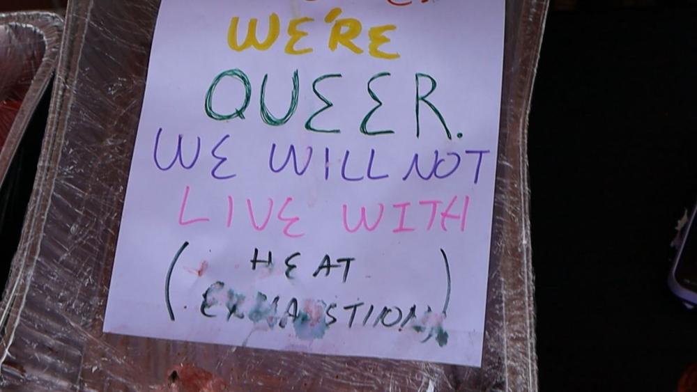 Hand-lettered sign reading We’re queer. We will not live with heat exhaustion.