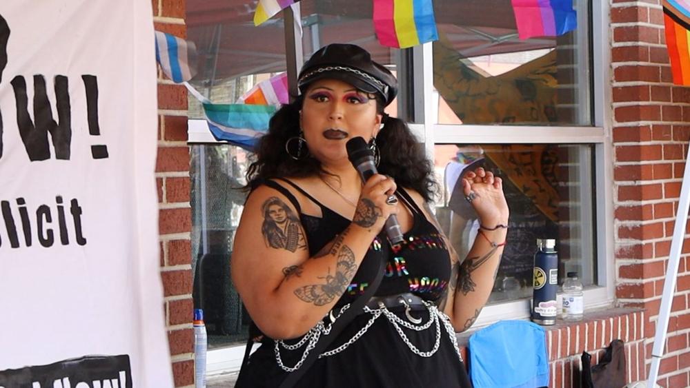 Dahlia speaking into a microphone under the coalition tent.